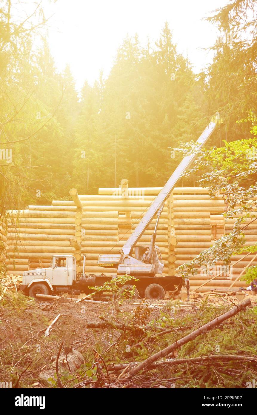Il processo di costruzione di una casa in legno da travi di legno di forma cilindrica. La gru in condizioni di lavoro Foto Stock