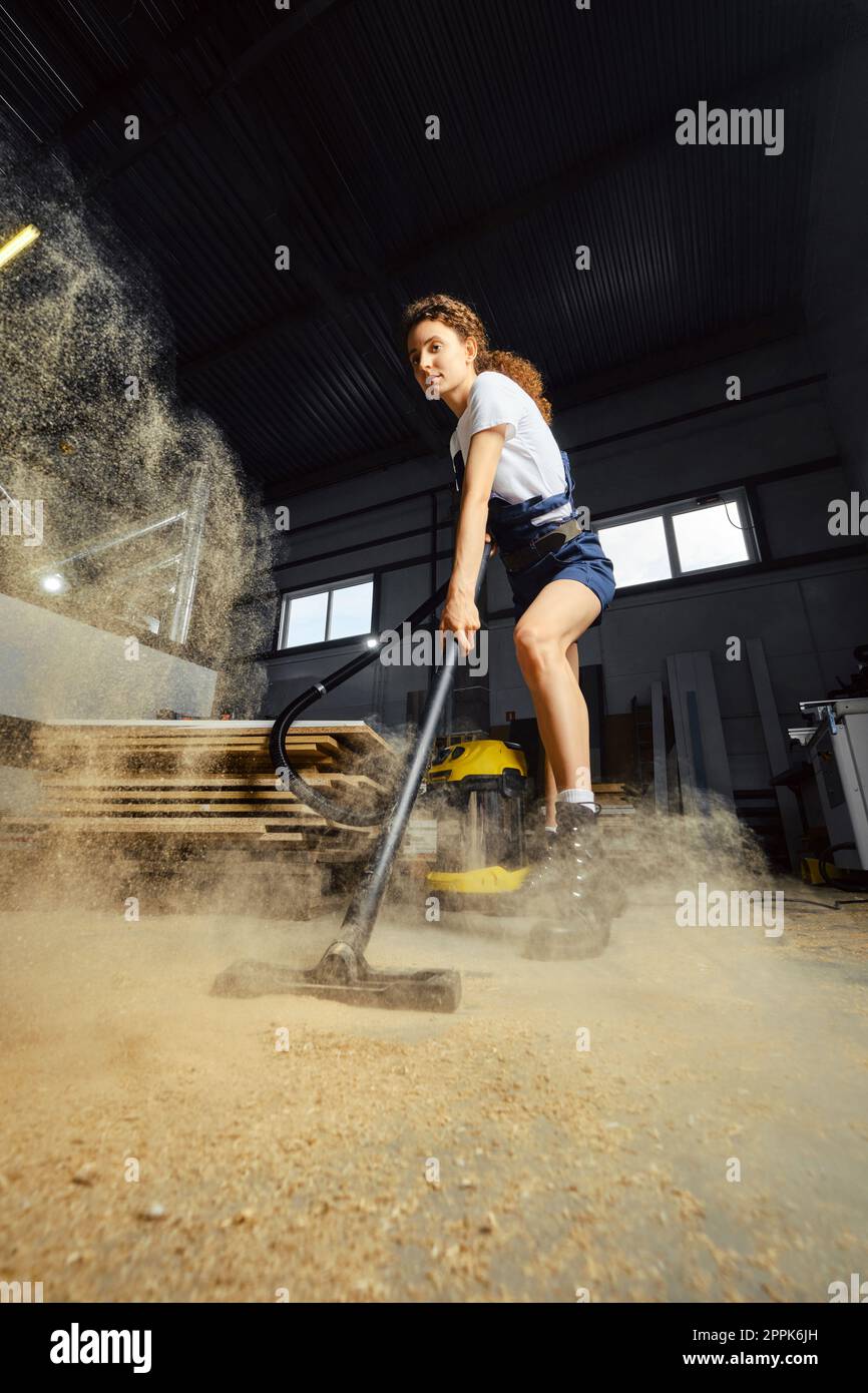 Giovane donna che utilizza l'aspirapolvere in un'officina di falegnameria Foto Stock