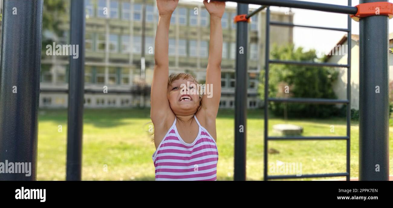 Sremska Mitrovica, Serbia, 15 settembre 2020 Un bambino con un vestito a righe pende su una barra di metallo e cerca di tirare le braccia. Sport o parco giochi. Palestra all'aperto. Foto Stock