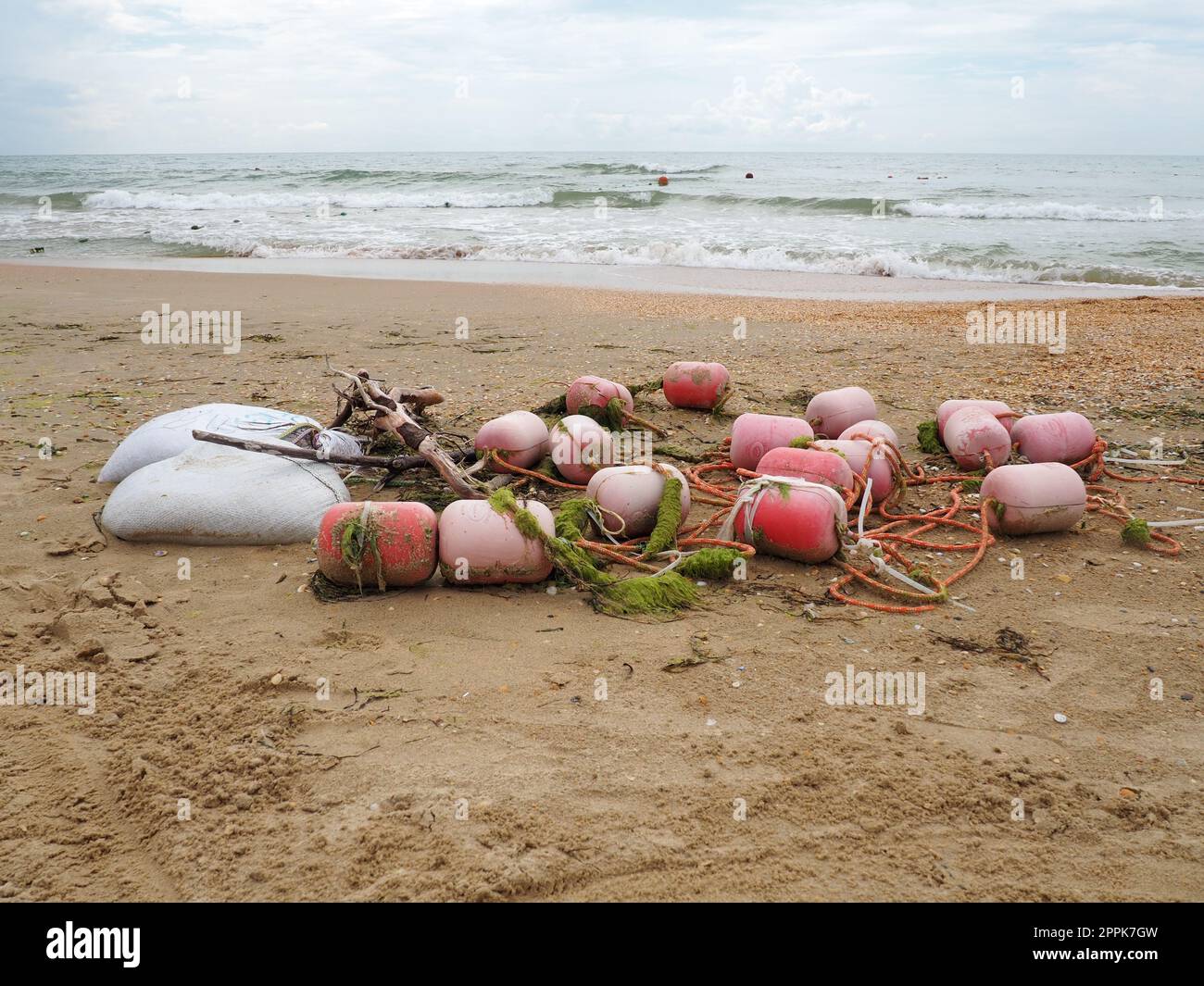 Boe nella sabbia. Una spiaggia bagnata con sabbia di quarzo grossolana. Corde aggrovigliate e boe di plastica lasciate sulla riva. Attrezzatura di sicurezza. La fine della stagione estiva. Tempo tempestoso in mare o in oceano. Bassa marea. Foto Stock