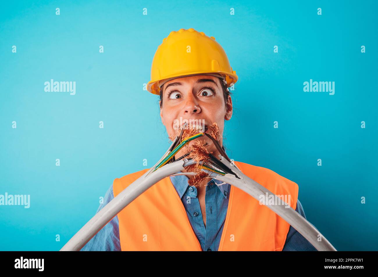 Scioccata ragazza operaia con casco rompe un cavo elettrico Foto Stock