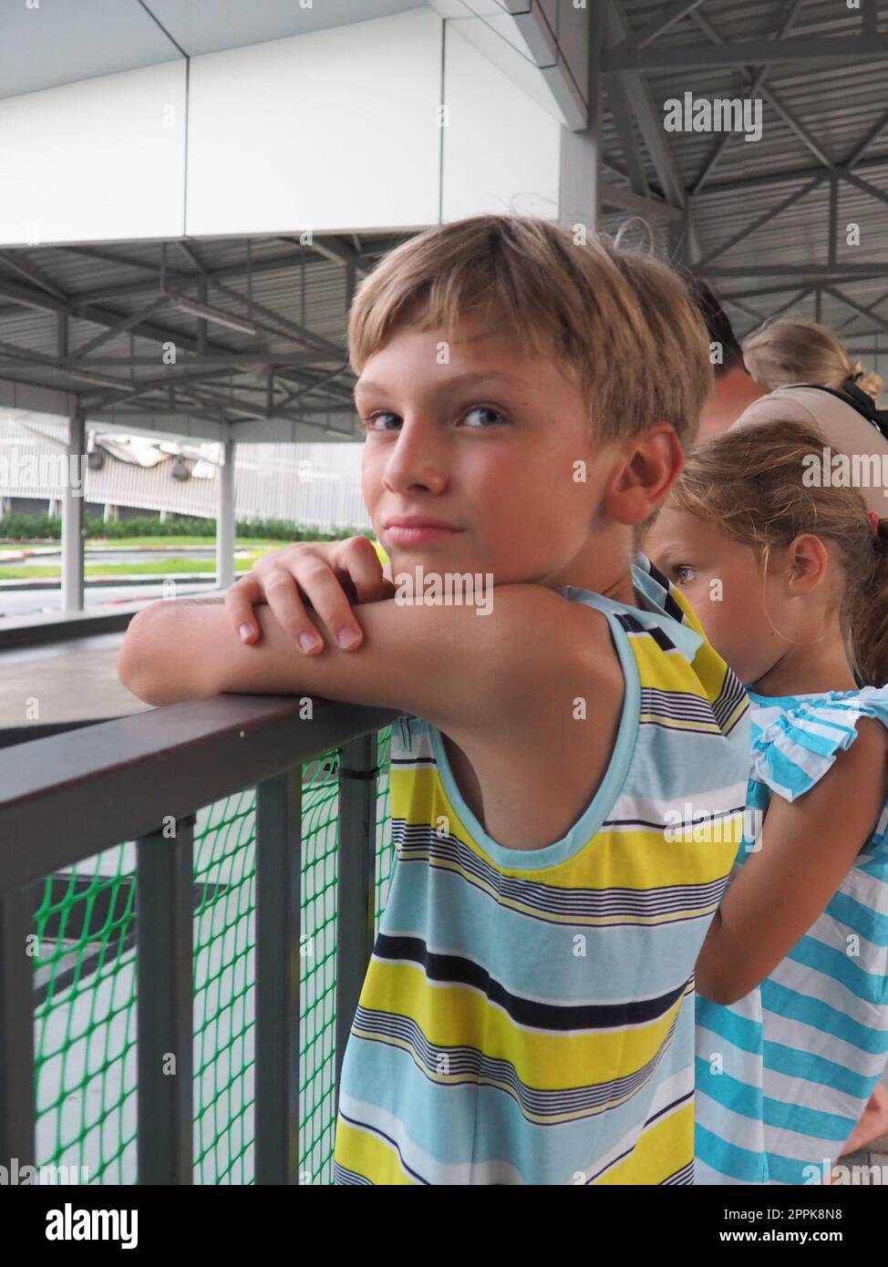 Anapa, Russia, 08.17.2021, ragazzo e ragazza allo stadio di karting. Il karting è uno sport e un intrattenimento, che gareggia su kart, con auto da corsa senza corpo. I bambini stanno alla recinzione. Eventi sportivi di gioco d'azzardo. Foto Stock