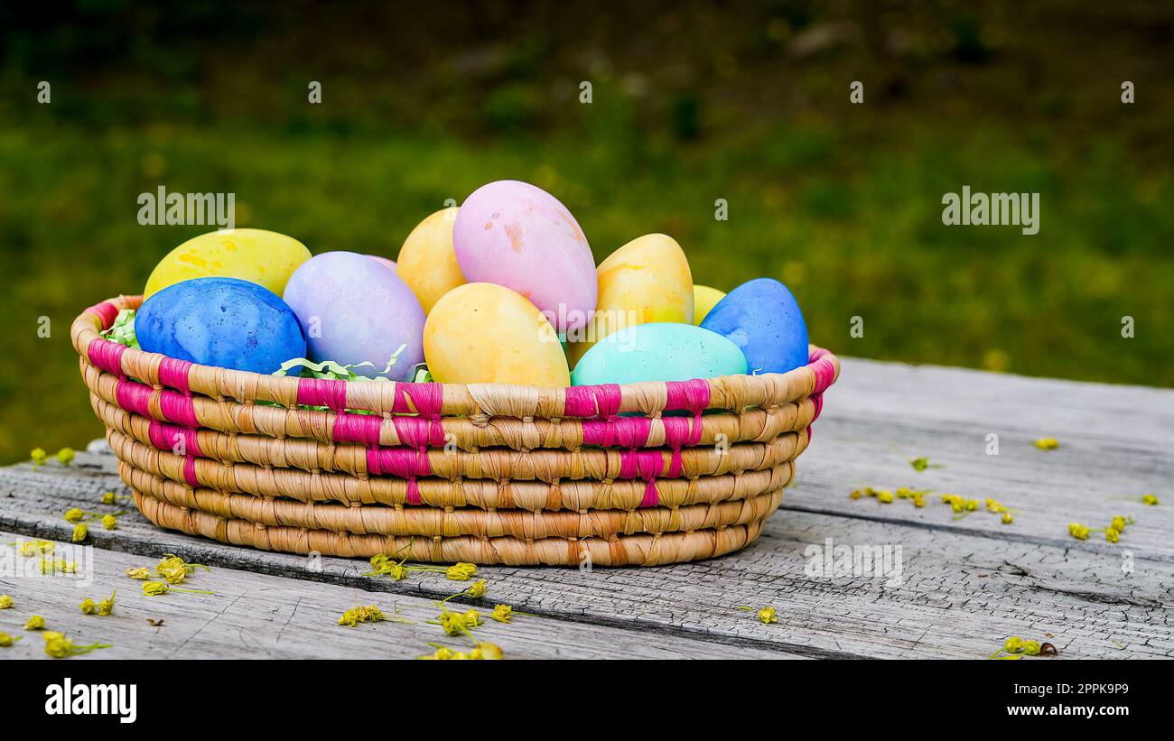 Uova di Pasqua colorate in piccolo cestino all'esterno sul tavolo Foto Stock