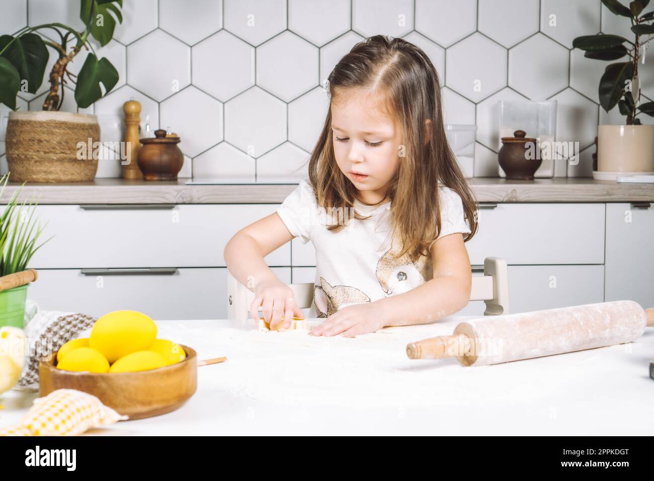 Ritratto di una piccola e seria cuoca, che aiuta a preparare i biscotti pasquali a forma di impasto. Biscotto in tazza per la farina di pasta da forno. Foto Stock