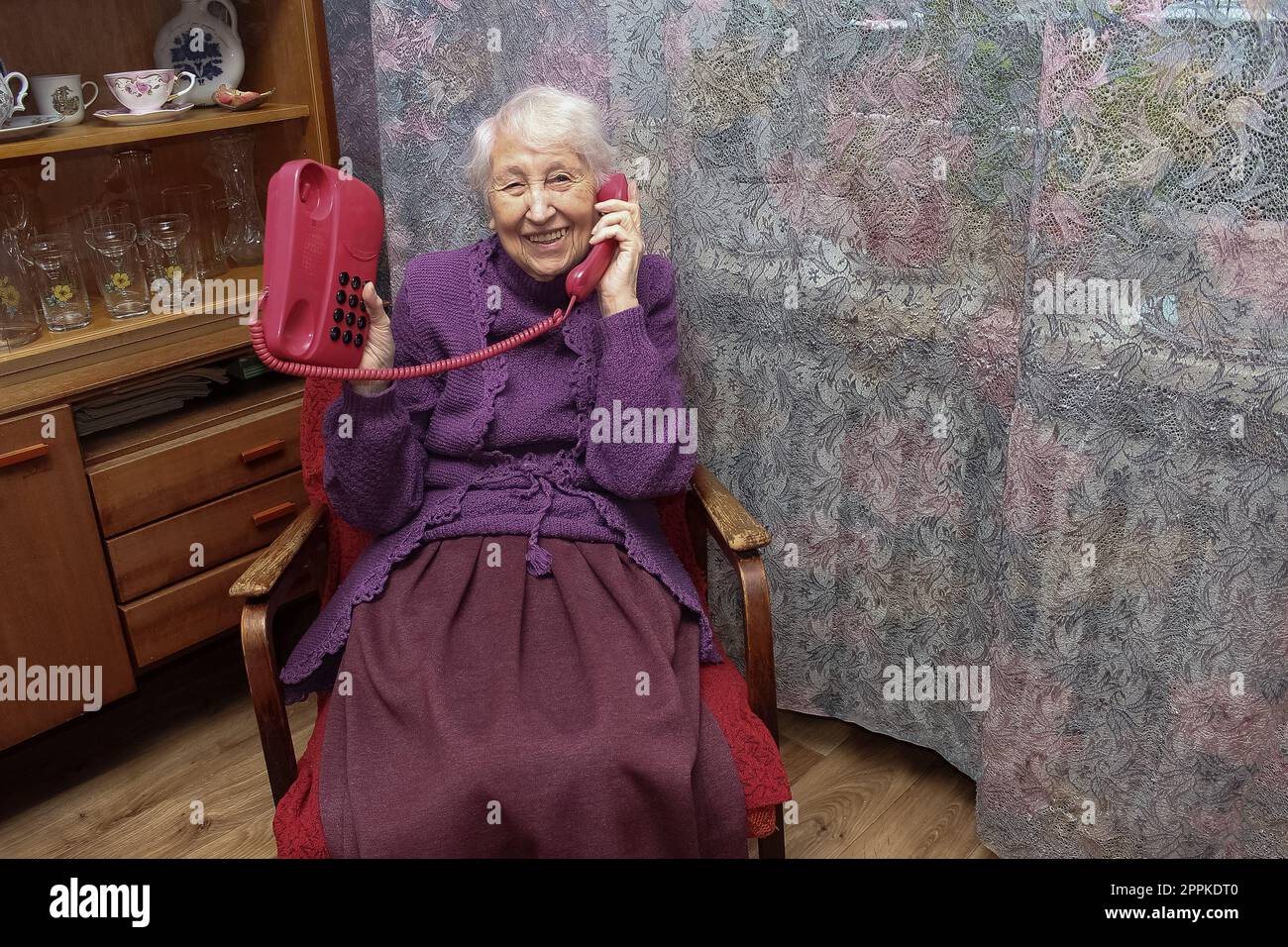 Donna anziana felice che usa il telefono fisso in stile retrò a casa Foto Stock