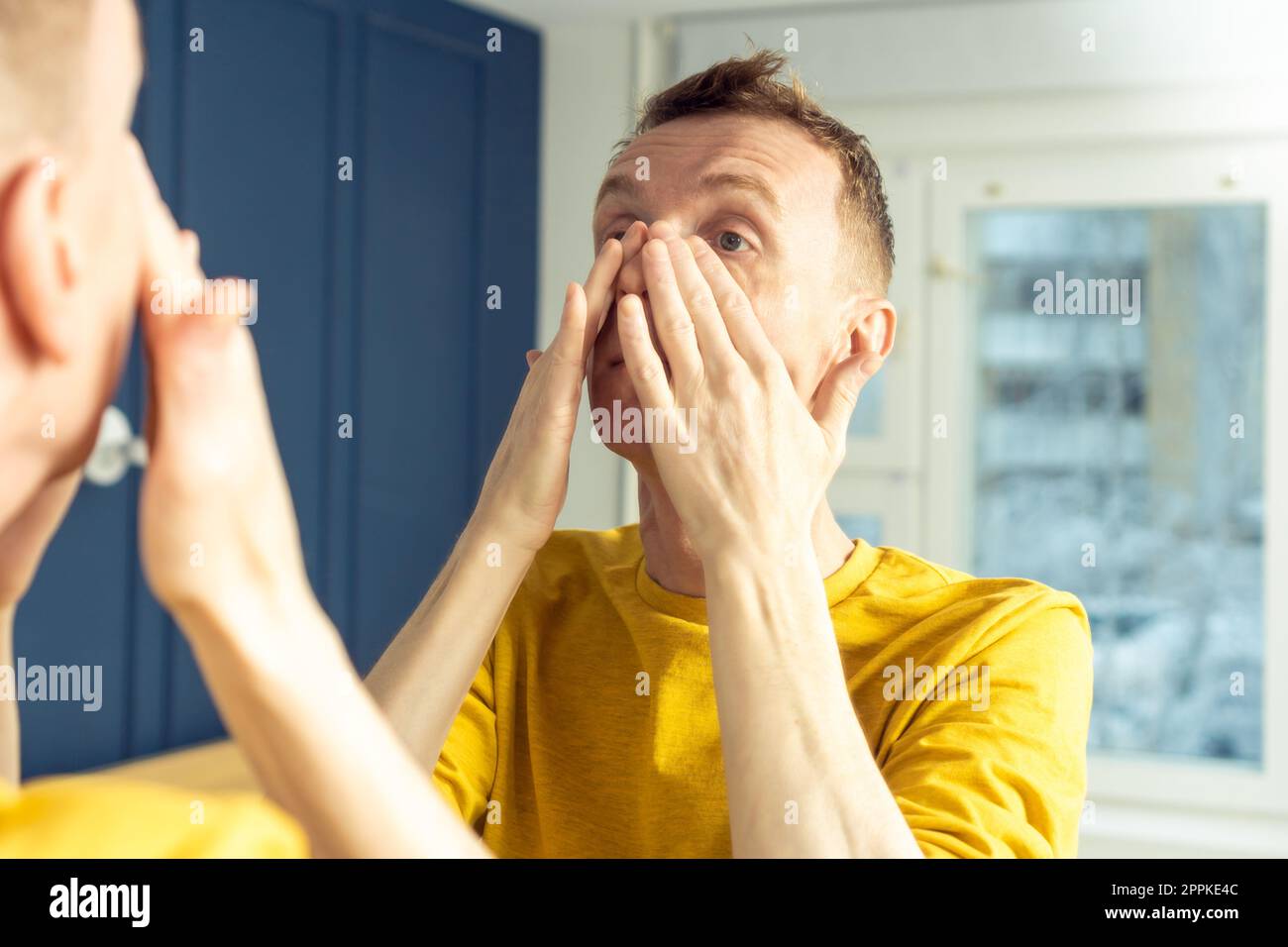 Uomo maturo applicare il prodotto cosmetico sul viso, quindi massaggiare con le mani. Ritratto maschile a specchio. Routine mattutina per la cura della pelle. Foto Stock