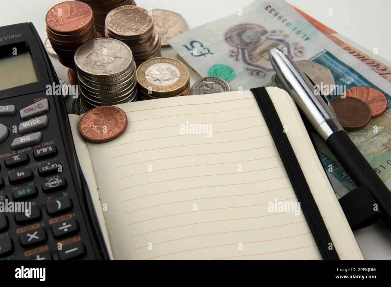 Pile di monete e banconote con calcolatrice, taccuino e penna Foto Stock