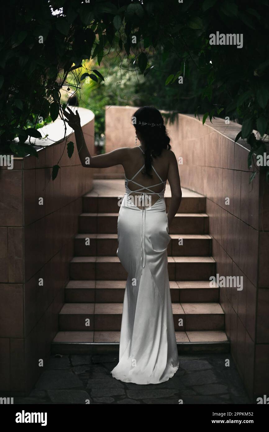 Primo piano elegante donna in lungo vestito bianco posa accanto alle scale concept foto Foto Stock