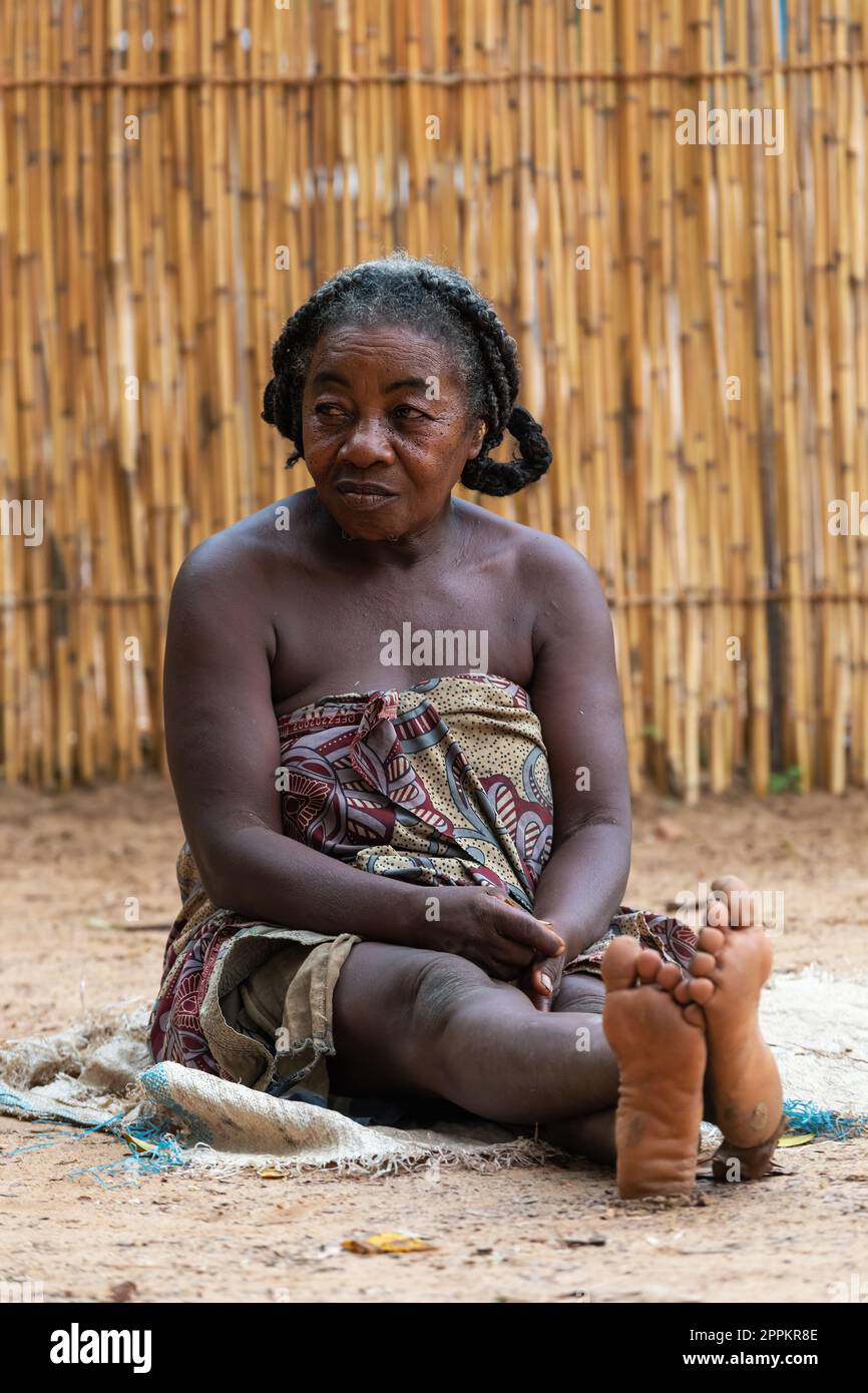Donna malgascia anziana che si rilassa di fronte alla capanna, non c'è alcuna opportunità di lavoro qui. La vita quotidiana nella campagna del Madagascar. Foto Stock
