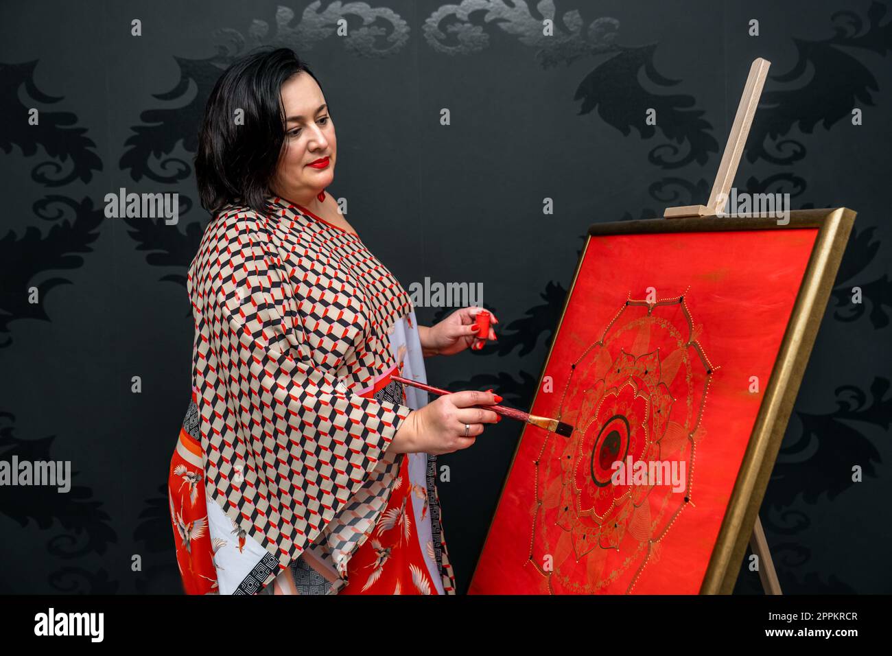 l'artista disegna un mandala con un pennello e una vernice rossa sulla tela Foto Stock