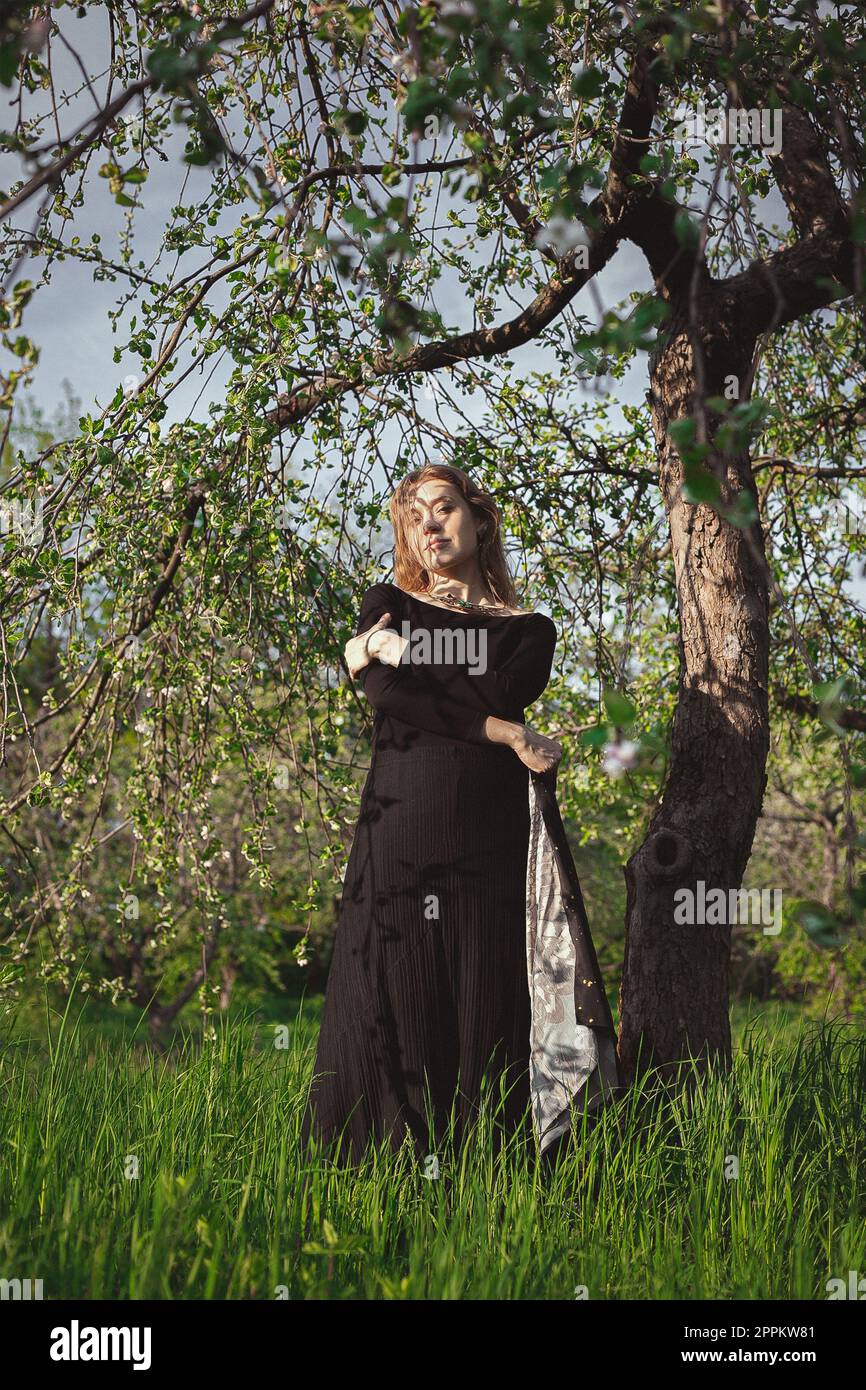 Donna in vestito nero sotto l'albero abbracciando se stessa fotografia panoramica Foto Stock