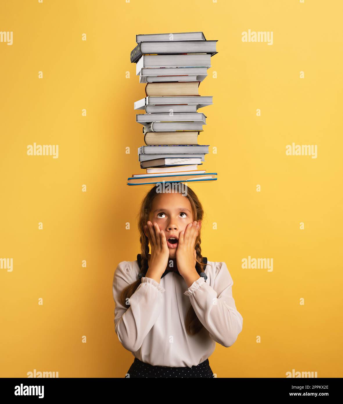 Un giovane bambino studente preoccupato a causa di una quantità eccessiva di libri da leggere e studiare. Sfondo giallo Foto Stock