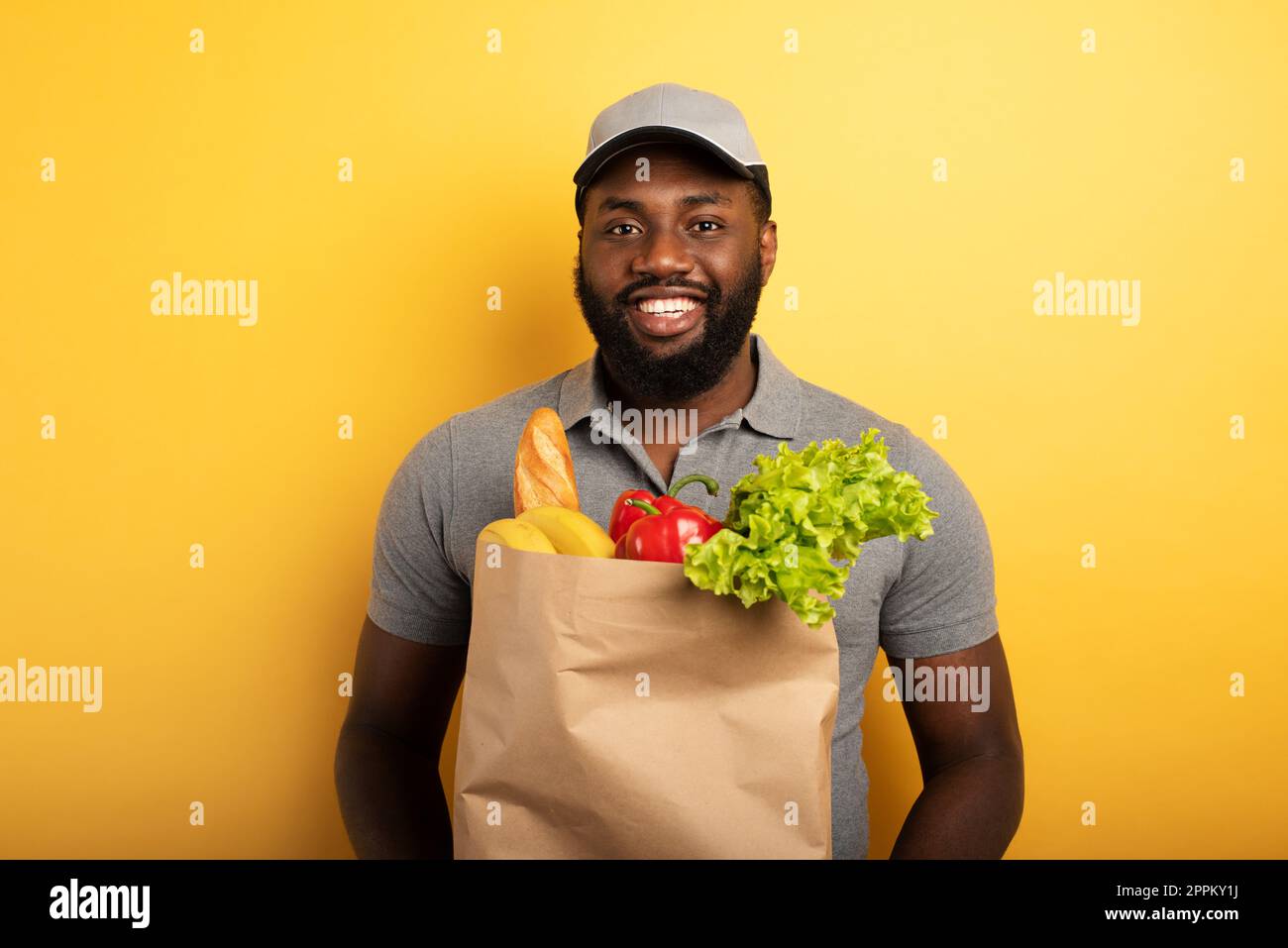 Deliveryman con espressione felice pronto a consegnare il sacchetto con il cibo. Sfondo giallo Foto Stock