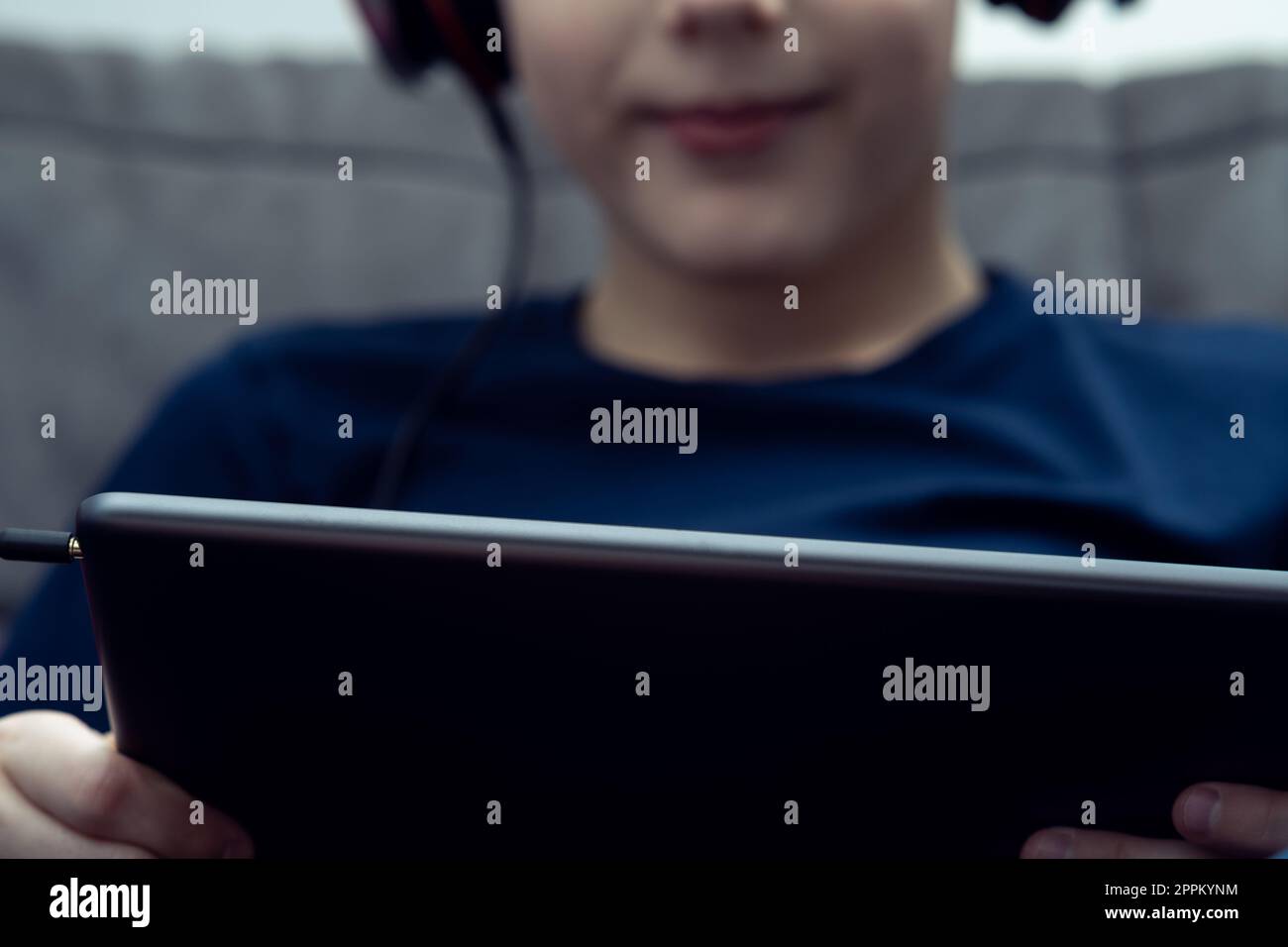 Ritratto di un ragazzo sorridente con primo piano del tablet digitale. I bambini in cuffie cablate giocano a videogame o guardano video. Foto Stock