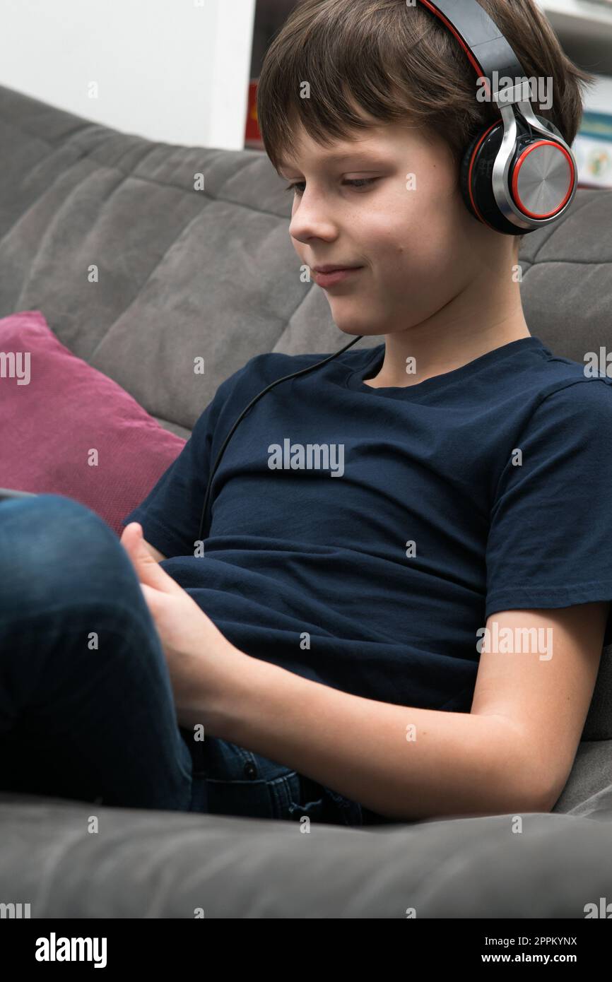 Ritratto di un bambino felice con un tablet digitale sul divano, vista laterale. Bambino in cuffie cablate. Foto Stock
