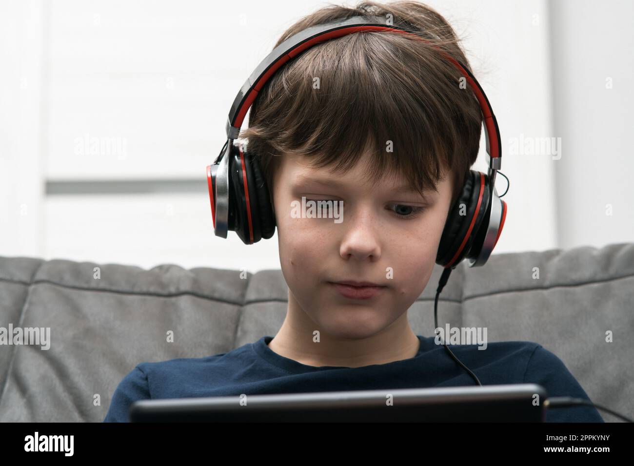 Ritratto di un ragazzo con un tablet digitale. I bambini con cuffie cablate giocano a videogame su gadget o ascoltano musica. Foto Stock