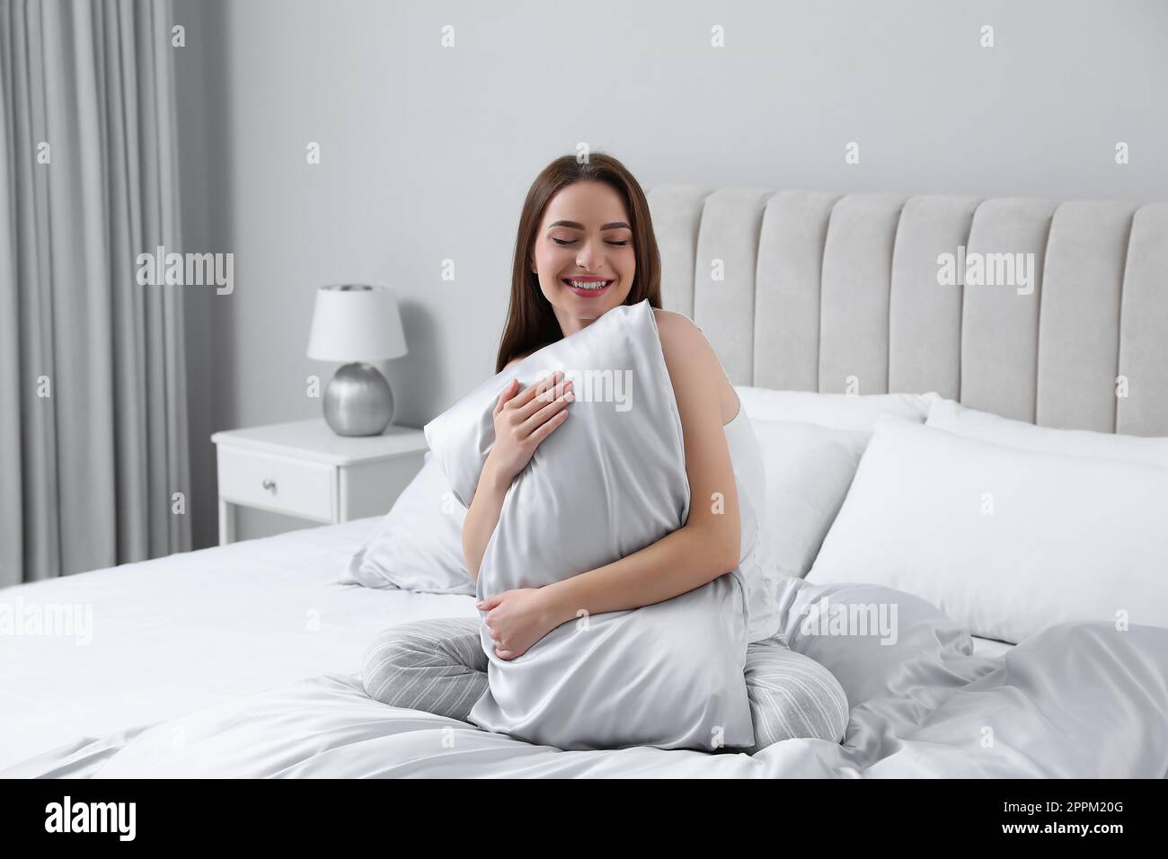 Giovane donna che abbraccia un cuscino su un comodo letto con lenzuola di  seta Foto stock - Alamy