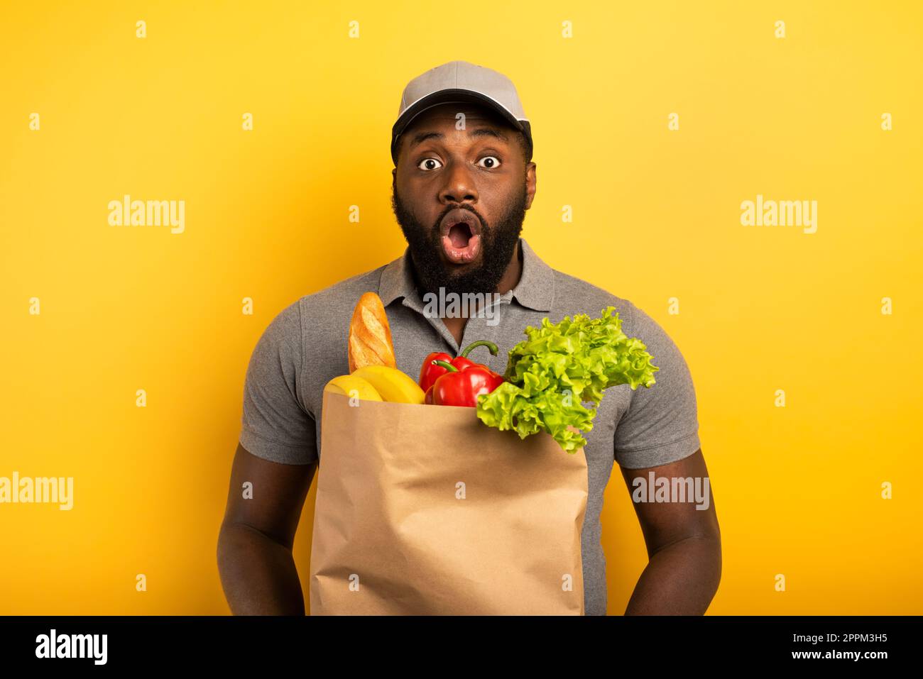 Deliveryman con espressione domandata pronta a consegnare il sacchetto con il cibo. Sfondo giallo. Foto Stock