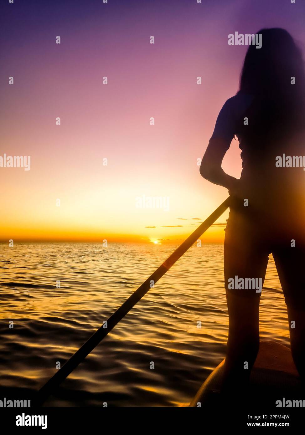 silhouette di una ragazza che pratica paddle surf in mare all'alba Foto Stock