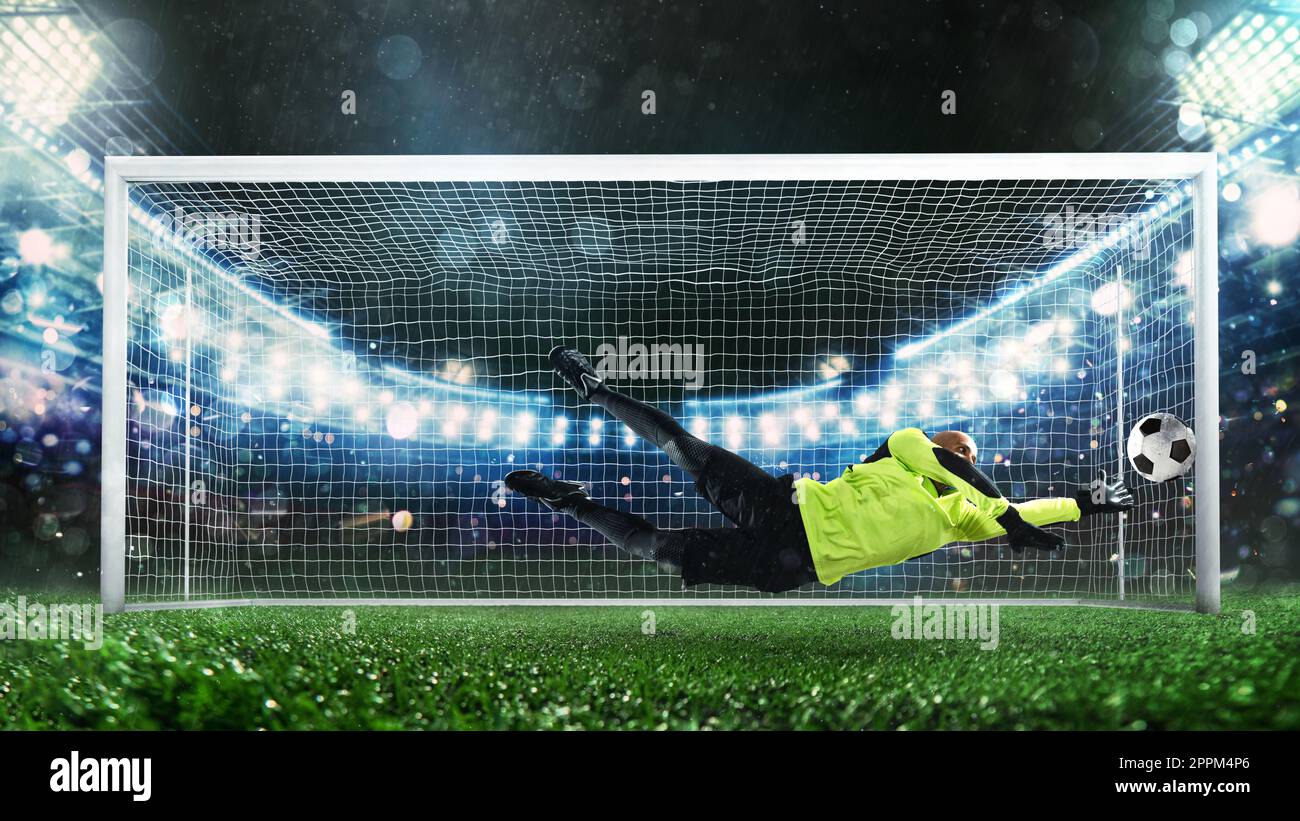 Portiere di calcio, in uniforme fluorescente, che fa un grande risparmio ed evita un gol durante una partita allo stadio Foto Stock