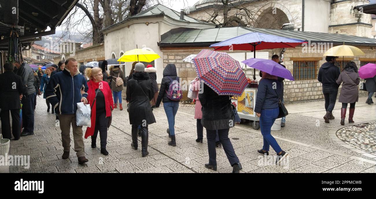 Sarajevo, Bosnia ed Erzegovina, 8 marzo 2020. Gente nelle strade centrali di Sarajevo. I turisti camminano intorno a Bascarsija. La moschea Gazi Husrev-begova dzamija. Persone con ombrelli Foto Stock