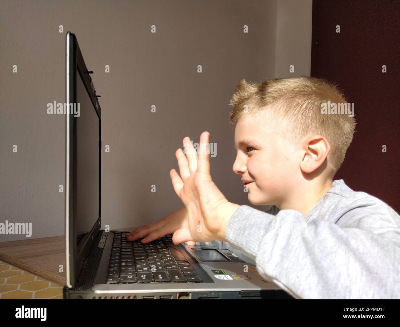 Sremska Mitrovica, Serbia, 20 maggio 2020 ragazzo biondo con portatile. Il bambino guarda il monitor e agita la mano come un saluto Foto Stock