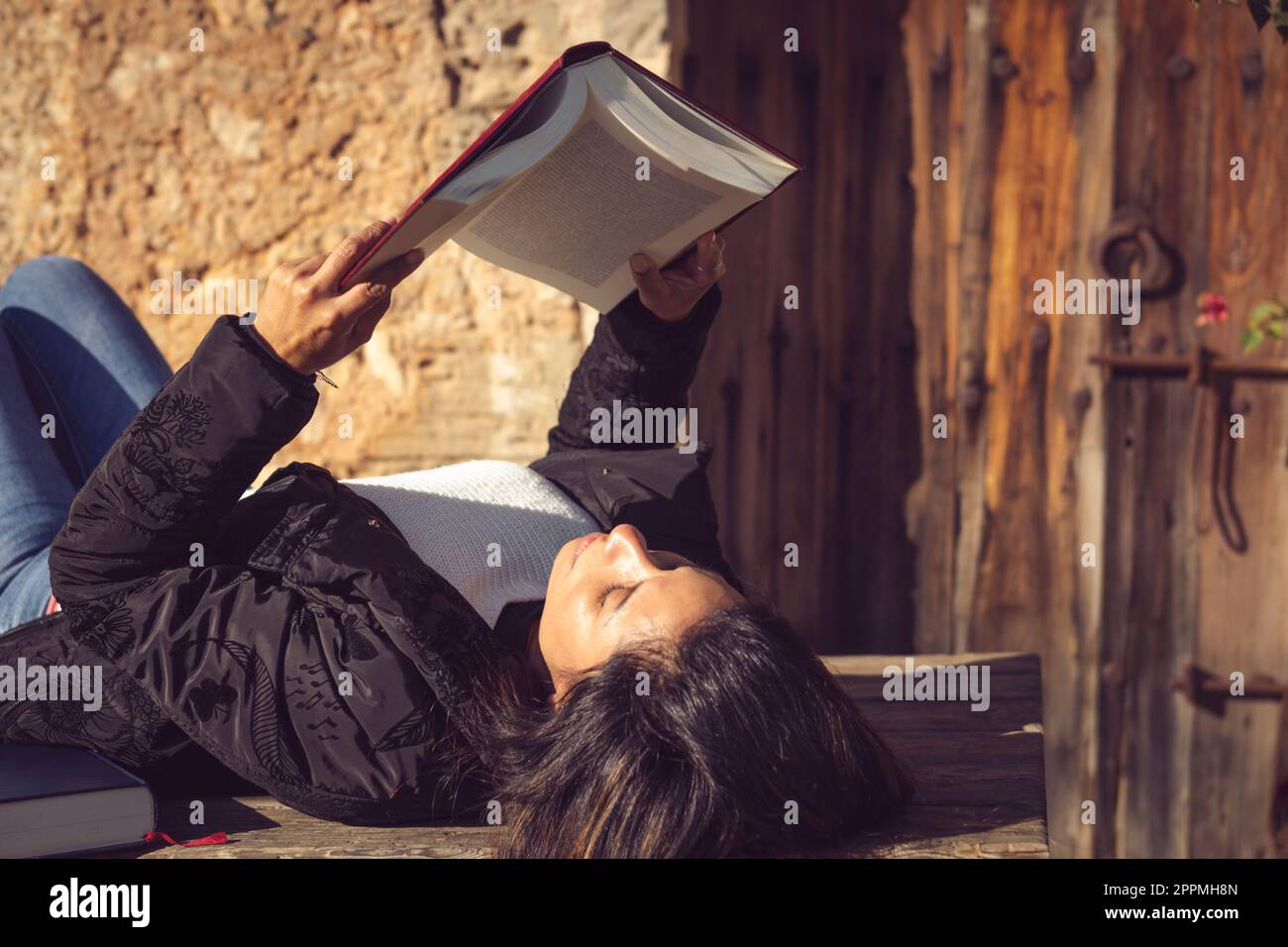 donna latina sdraiata, leggendo un libro in giardino Foto Stock