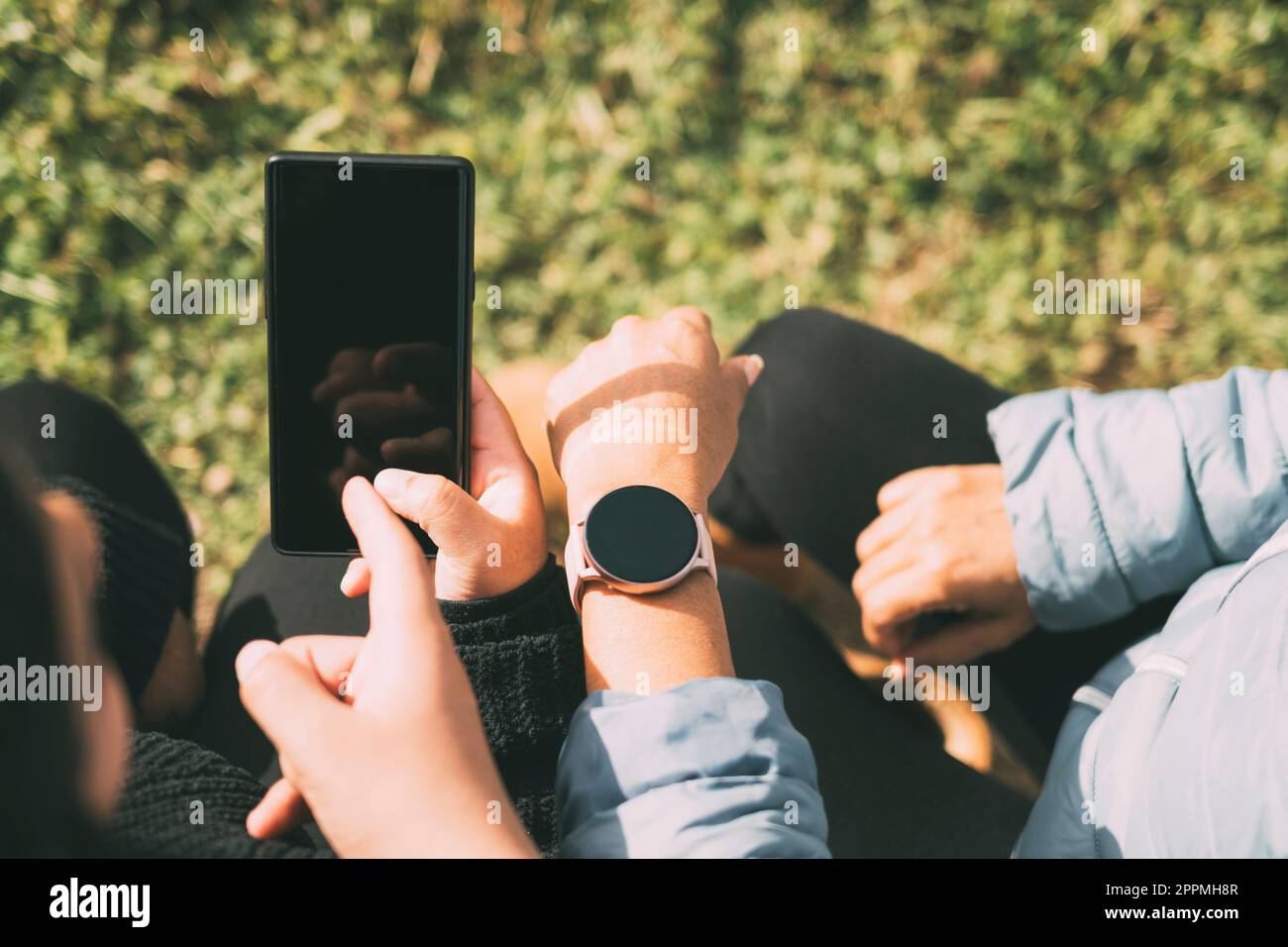 Adolescente maschio ispanico in possesso di smartphone guardando lontano mentre si siede in erba con madre ispanica e sorella in parco il giorno di sole Foto Stock