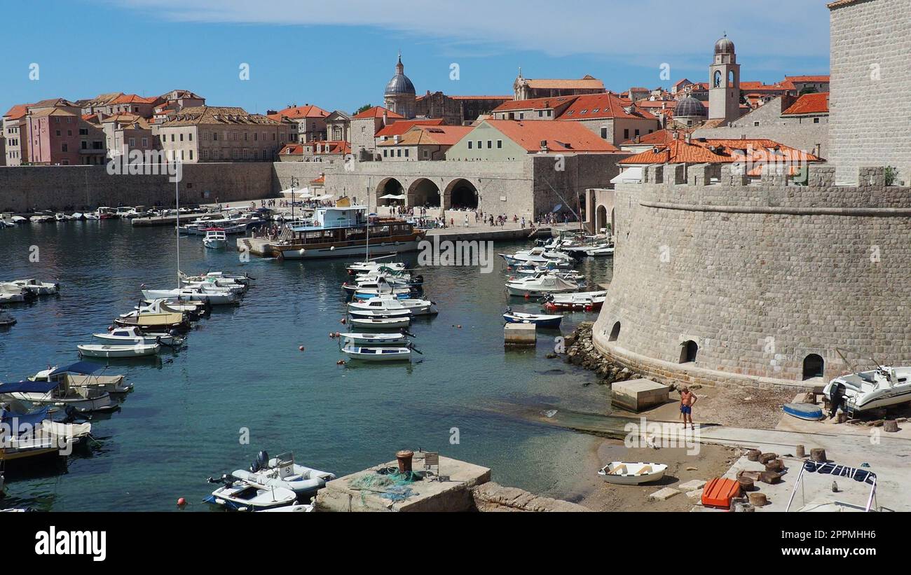 Dubrovnik, Croazia, 14 agosto 2022. Porto cittadino in estate, attrazione turistica. I turisti camminano, salgono su barche e navi e fanno gite in barca. Mare Adriatico. Un abitante del posto gioca con un cane. Vecchi forti. Foto Stock