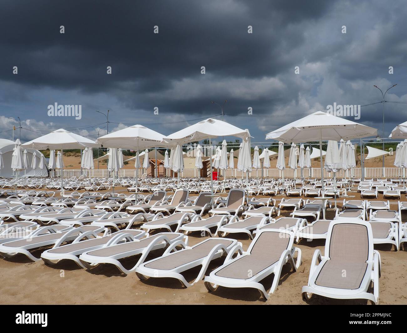 Anapa, Russia, 15 agosto 2021 lettini e ombrelloni bagnati sulla spiaggia di mare durante una forte tempesta di pioggia. Ombrellone arrotolato sulla spiaggia contro il cielo nuvoloso scuro. Invasione di un tifone, ciclone o tempesta Foto Stock