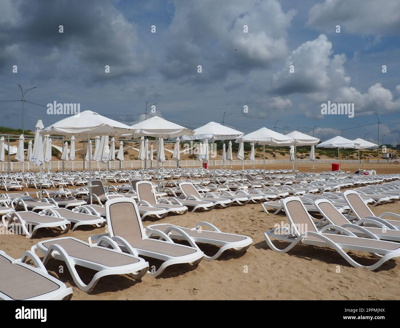 Anapa, Russia, 15 agosto 2021 lettini e ombrelloni bagnati sulla spiaggia di mare durante una forte tempesta di pioggia. Ombrellone arrotolato sulla spiaggia contro il cielo nuvoloso scuro. Invasione di un tifone, ciclone o tempesta Foto Stock