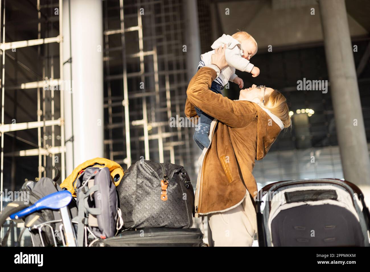 Motherat è felice di tenere e sollevare il bambino in aria dopo essere stato riunito di fronte alla stazione del terminal dell'aeroporto. Concetto di viaggio per bambini. Foto Stock