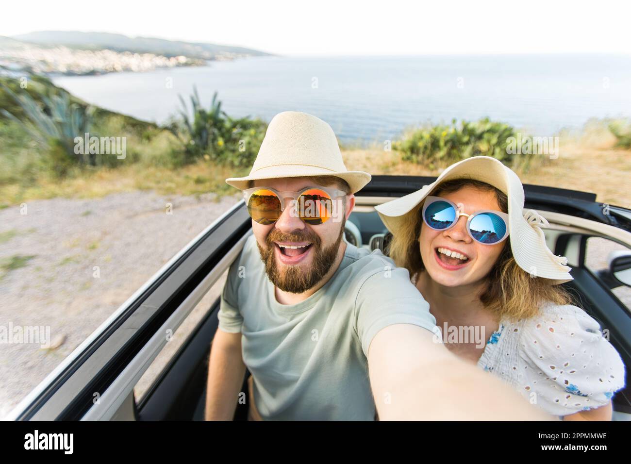 Una coppia romantica che fa selfie con la fotocamera dello smartphone in una cabrio a noleggio sull'oceano o sulla spiaggia di mare, mentre si gode una vacanza estiva insieme e si scatta una foto sul cellulare che riposa vicino al mare nei fine settimana Foto Stock