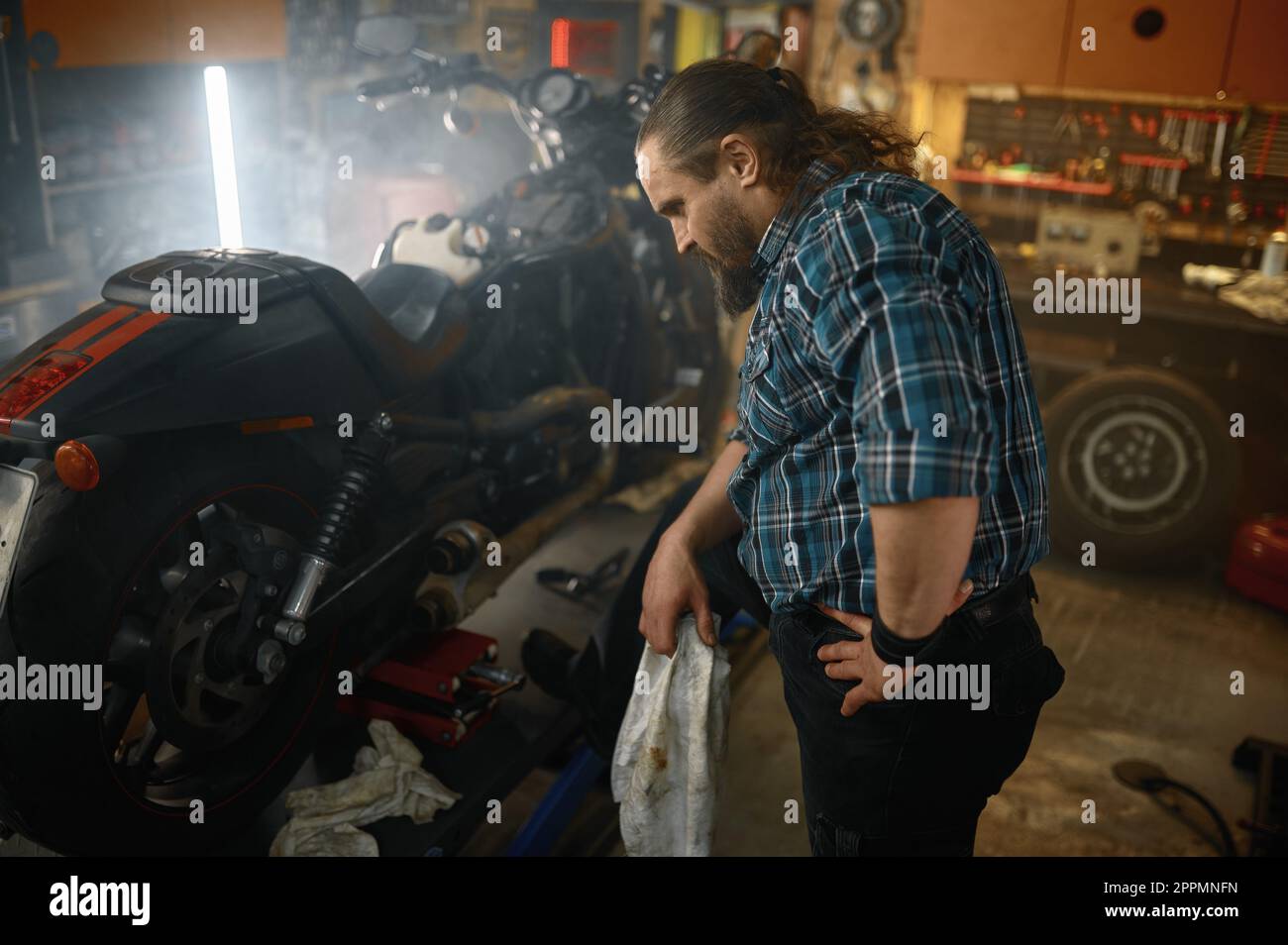 Brutale biker strofinando le mani durante la riparazione del motore di motocicletta Foto Stock