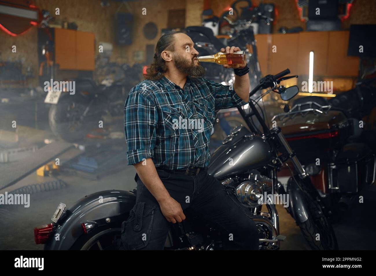 Uomo stanco biker bere birra dalla bottiglia dopo duro lavoro di riparazione in garage Foto Stock