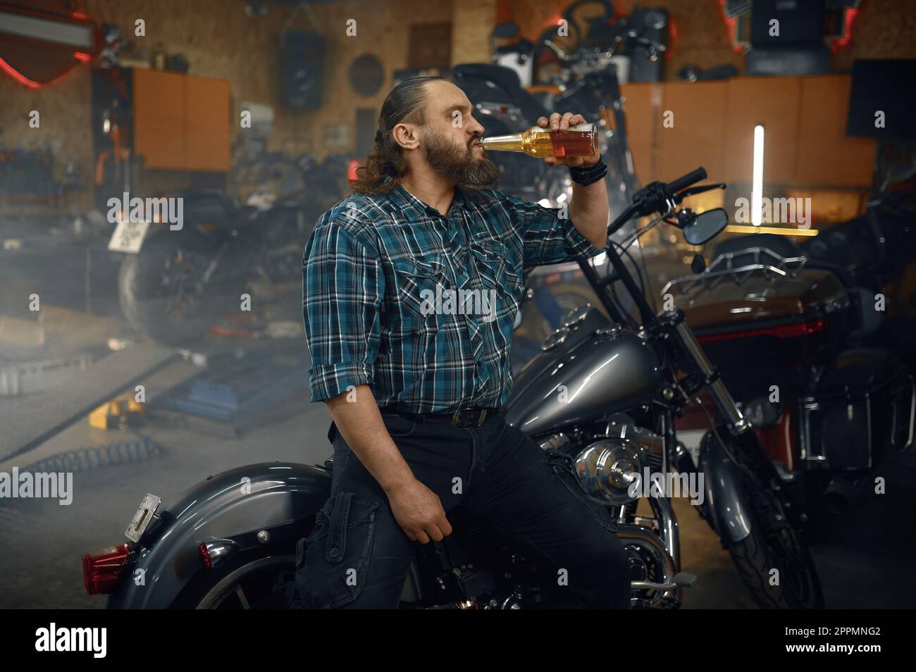 Uomo stanco biker bere birra dalla bottiglia dopo duro lavoro di riparazione in garage Foto Stock