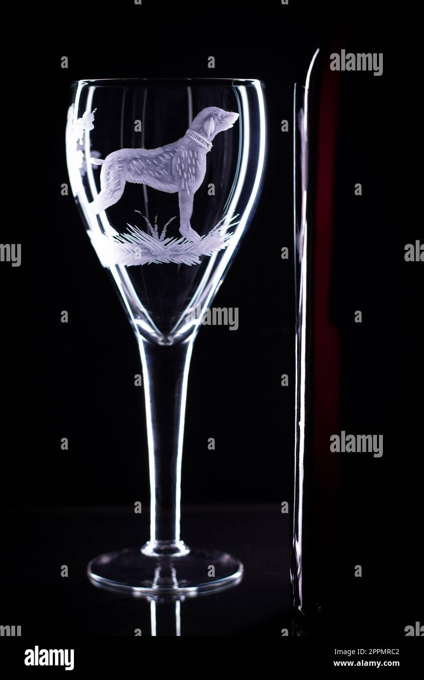 Bicchiere di vino con un cane sabbiato e una bottiglia di vino su sfondo nero. Copia spazio Foto Stock
