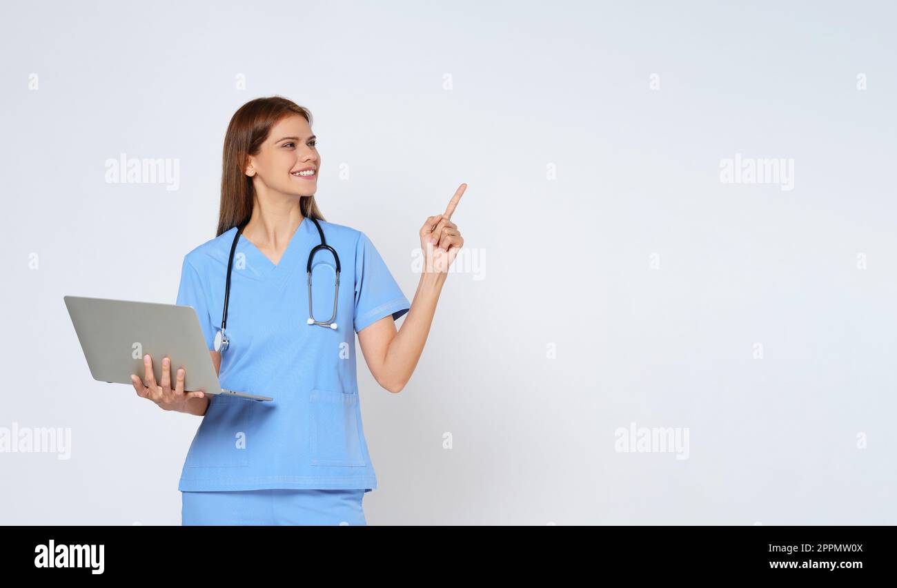 Ritratto di giovane donna sorridente dottore con stetoscopio che tiene il portatile e che punta con la mano su copia spazio isolato su sfondo bianco. Foto Stock