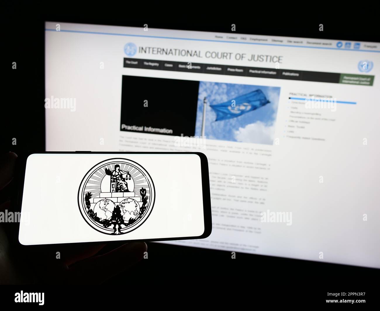 Persona che tiene uno smartphone con il logo della Corte internazionale di giustizia (ICJ) sullo schermo di fronte al sito Web. Messa a fuoco sul display del telefono. Foto Stock