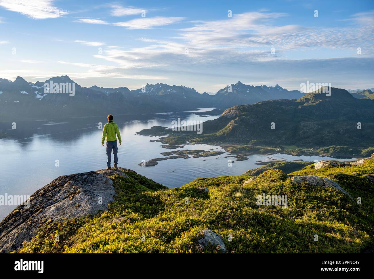 Escursionista che guarda in lontananza, Fjord Raftsund e le montagne nella luce della sera, vista dalla cima di Dronningsvarden o Stortinden, Vesteralen Foto Stock