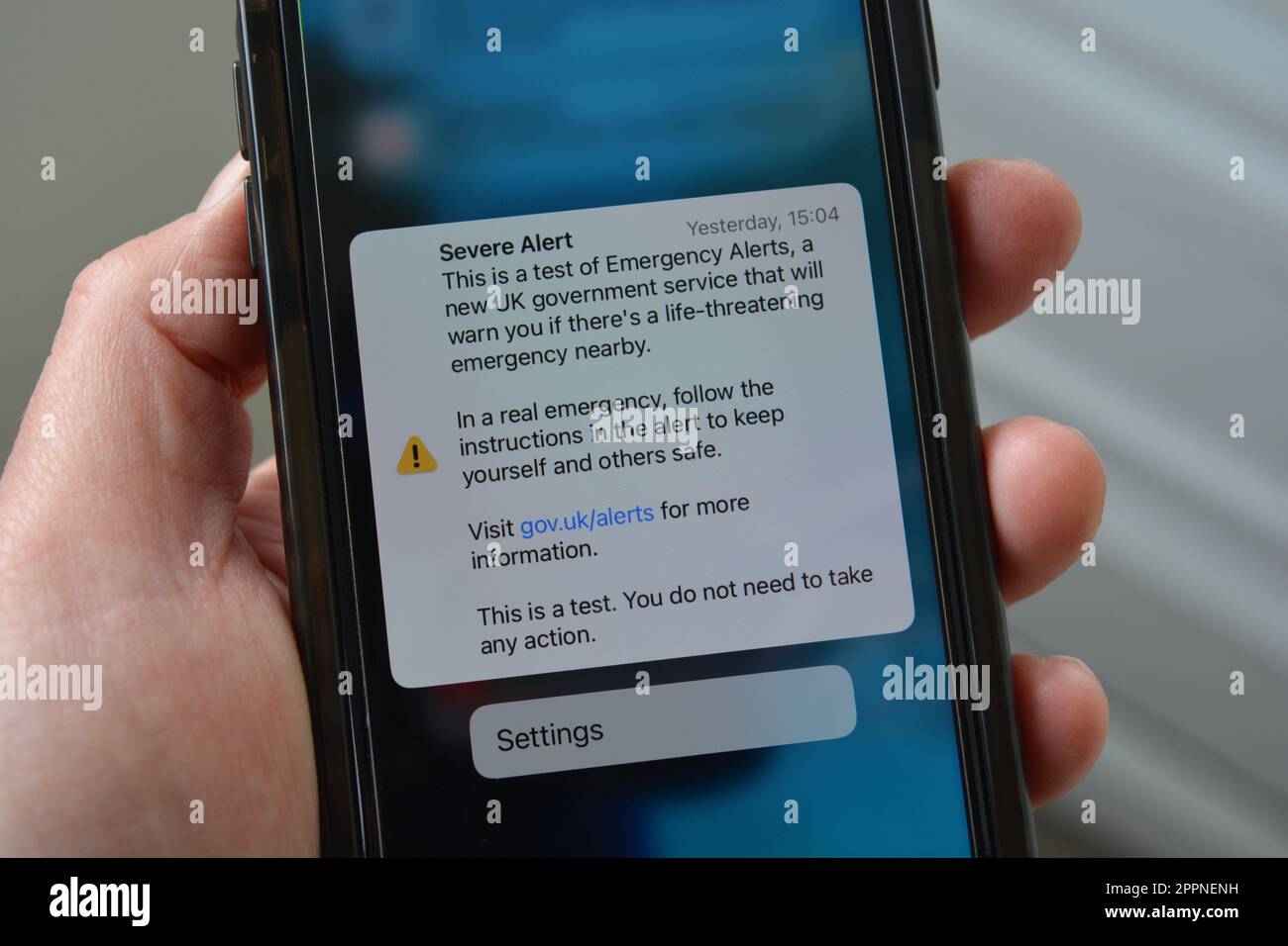 Cellulare in mano con schermo che mostra il testo di prova per allarme grave, questo è un test di emergenza allarmi, un nuovo servizio governativo Foto Stock