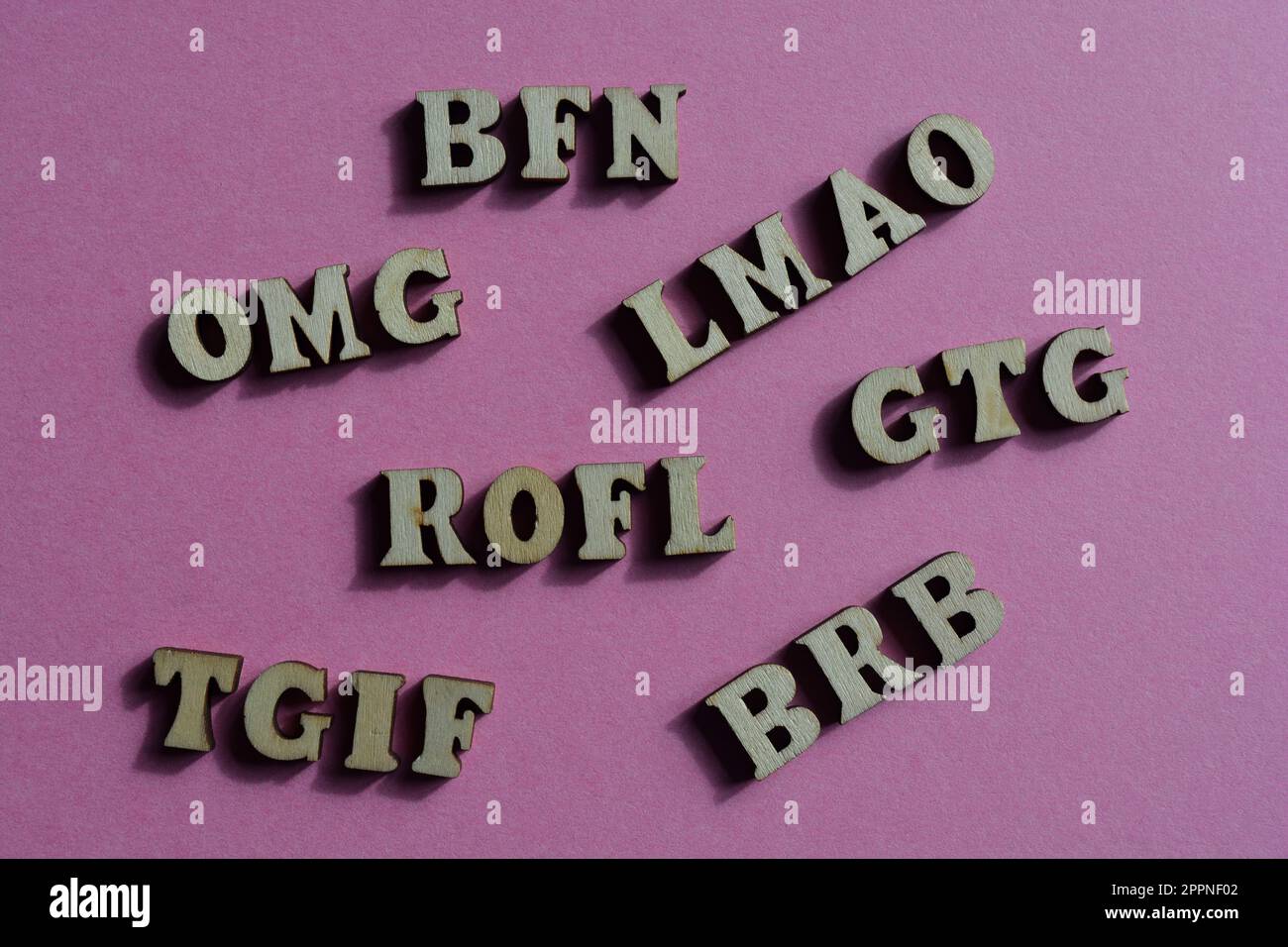 Acronimi, tra cui BRB, Be Right Back e BFN, Bye for Now, in lettere alfabetiche di legno isolate su sfondo rosa Foto Stock