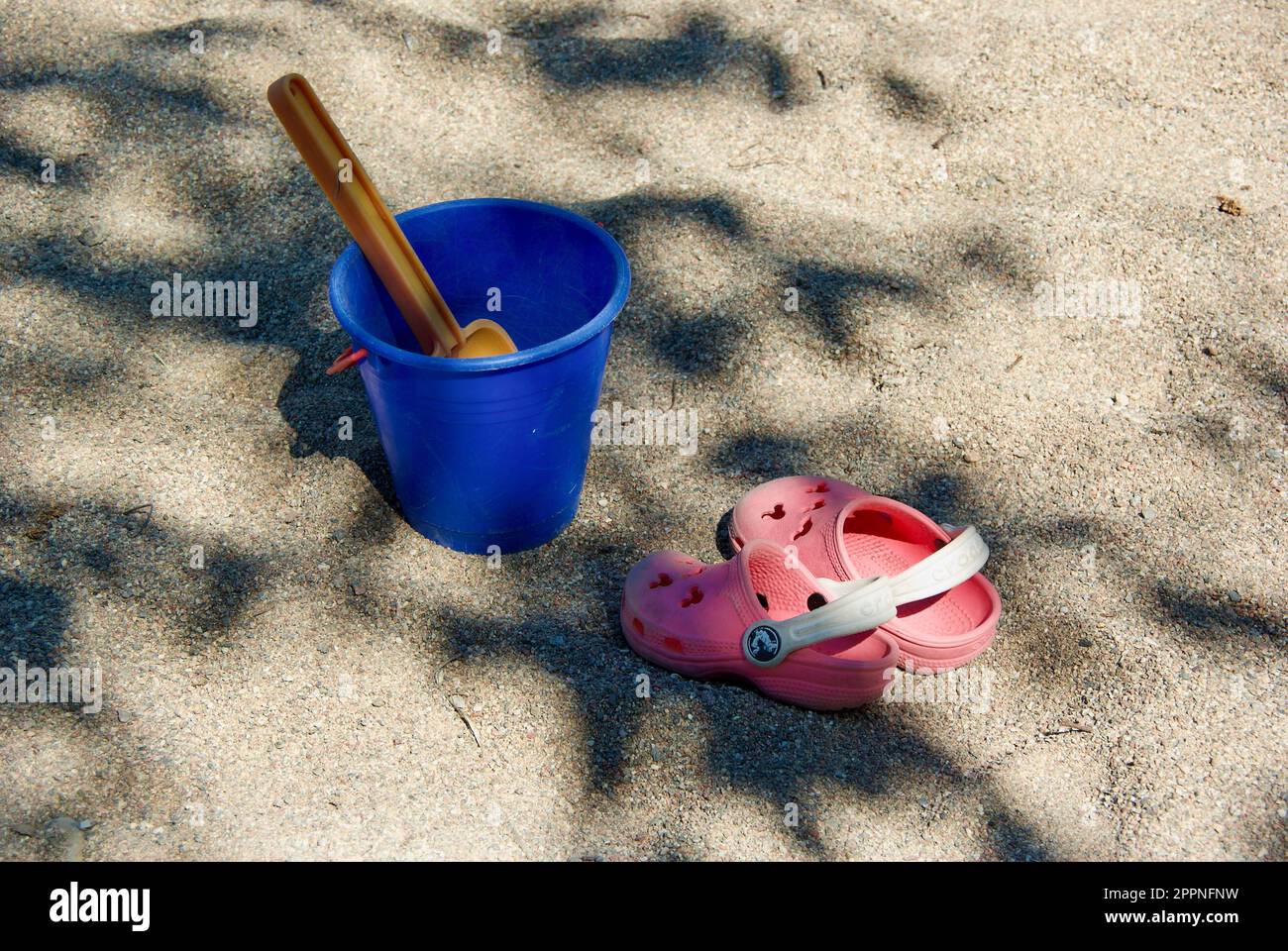 Giocattoli di sabbia all'aperto e un paio di sandali nel sandbox all'ombra di un albero in estate. Foto Stock