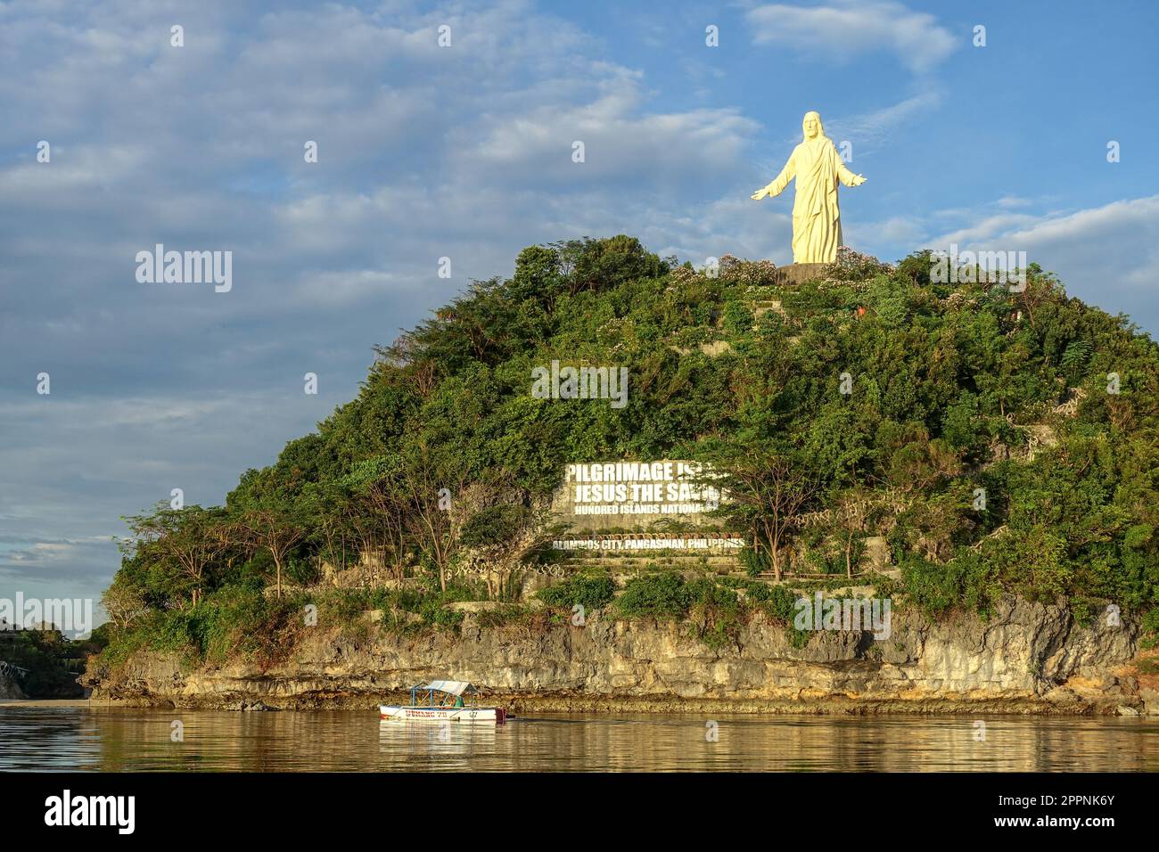 Grande statua di Gesù Cristo che si affaccia sull'acqua con una barca sotto e un cartello per il pellegrinaggio sotto la statua, cento isole, Filippine Foto Stock
