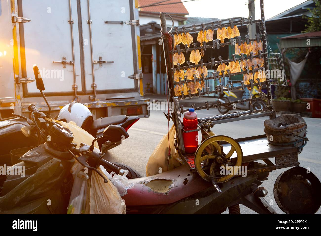 Il calamaro secco pressato appende da un supporto montato su una moto di un venditore di strada alla luce del tramonto, Thailandia Foto Stock