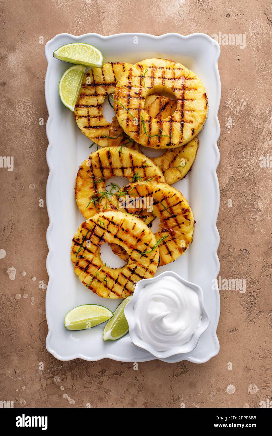 Ananas alla griglia con glassa al miele di lime, scorza di lime e panna montata su un piatto da portata sopra Foto Stock