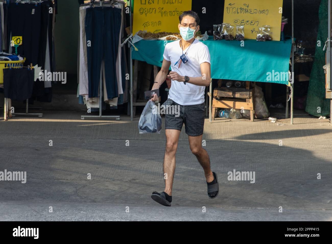 SAMUT PRAKAN, THAILANDIA, Apr 07 2023, Un uomo con una maschera sul suo viso corre lungo la strada accanto al mercato Foto Stock