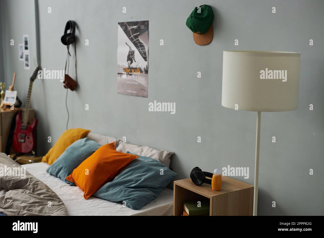Parte della camera da letto con cappellino e poster appesi alla parete grigia con comodo letto matrimoniale con gruppo di morbidi cuscini multicolore Foto Stock
