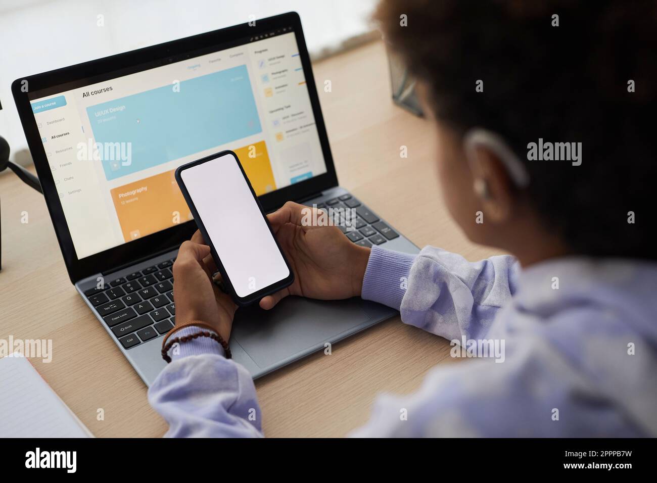 Primo piano dello smartphone con schermo vuoto tenuto da un adolescente davanti allo schermo del computer portatile con la home page del sito Web per l'apprendimento a distanza Foto Stock