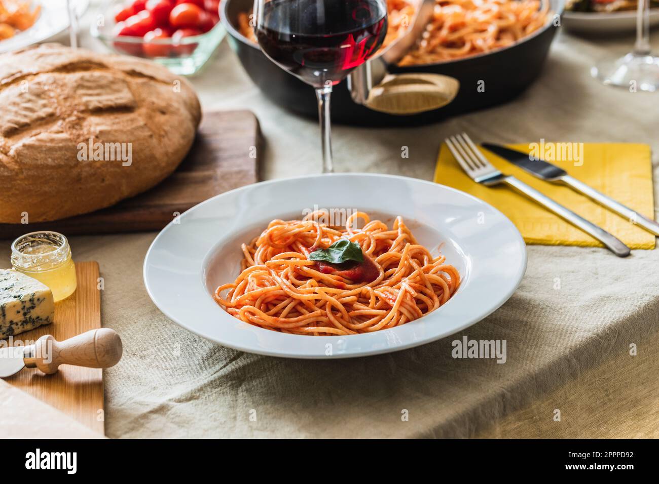 Tavolo con focalizzazione selettiva su un piatto di spaghetti con salsa di pomodoro. Pane, posate e bicchiere di vino rosso sullo sfondo Foto Stock